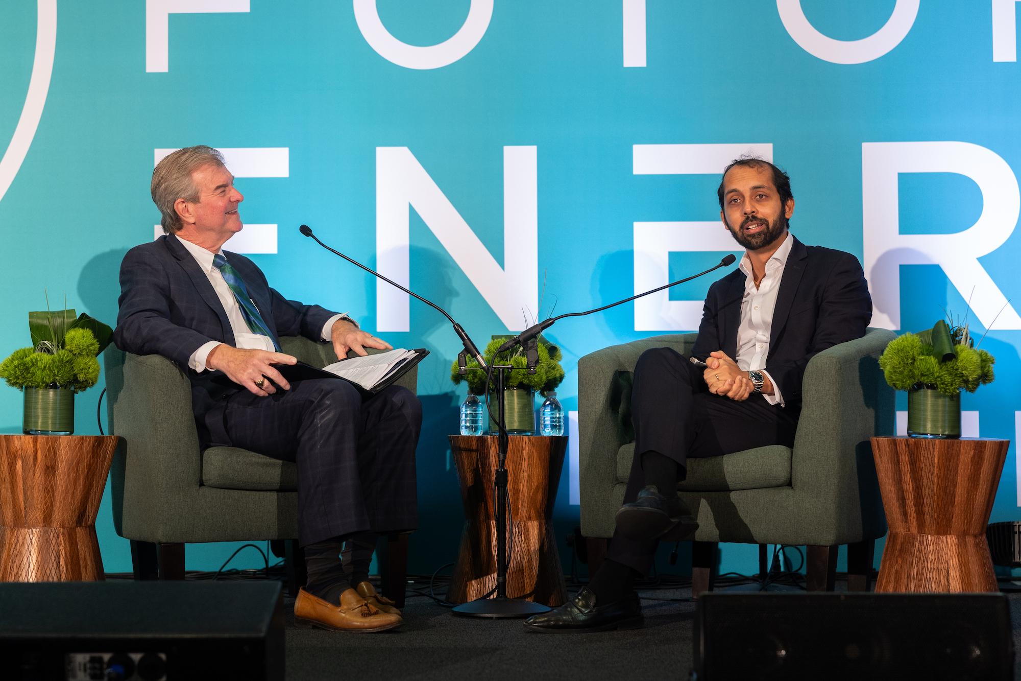 Host and guest sitting in arm chairs talking into microphones