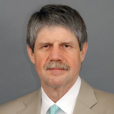 Close-up headshot of a man, focusing on his facial features and expression, with a neutral background softly blurred behind her.