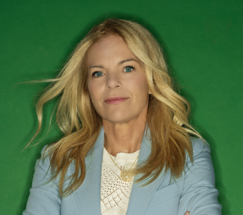 Close-up headshot of a woman, focusing on her facial features and expression, with a neutral background softly blurred behind her.